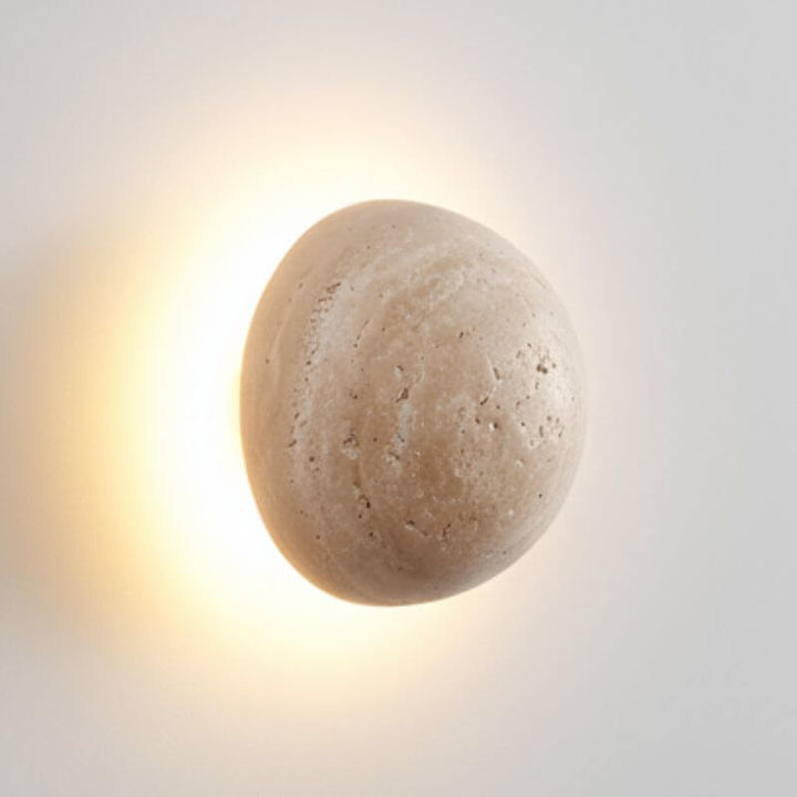 Arandela de Parede Travertino Soleil em formato esférico com luz amarelada em fundo branco profissional para cliente sofisticados