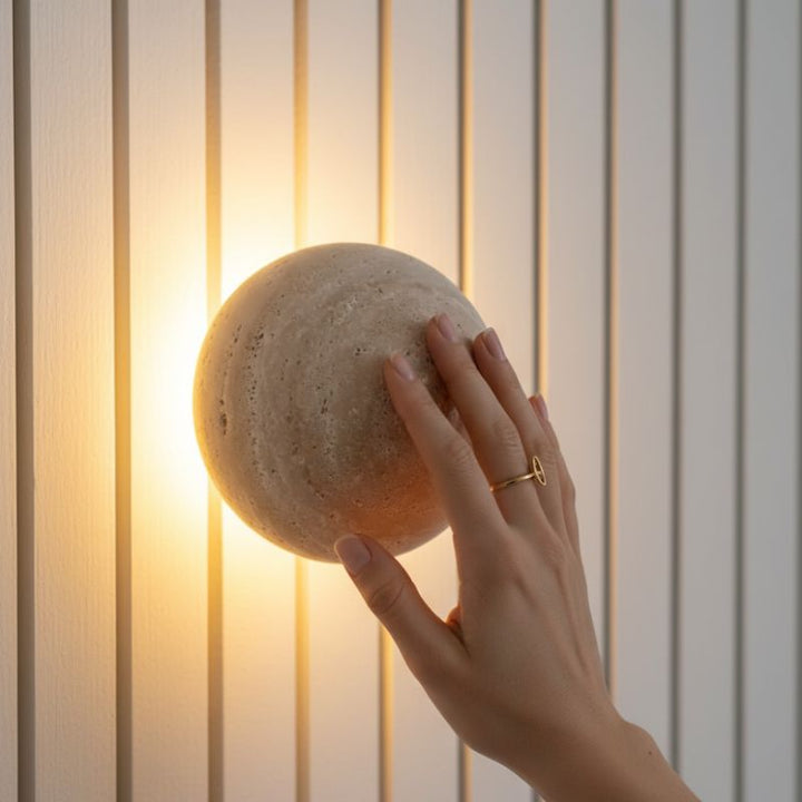 Arandela de Parede Travertino Soleil instalada com uma mão sentindo a textura