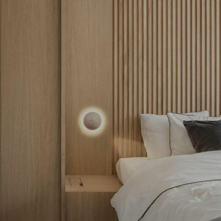 Arandela de Parede Travertino Soleil em formato esférico com luz amarelada em fundo com parede ripado ao lado de uma cama